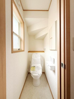 窓から自然光が差し込む明るいトイレです。棚や収納スペースも備わっておりすっきりとした内装が魅力です。天井のデザインが空間にアクセントを与えています。ホワイト基調で清潔感のある印象を持てます。