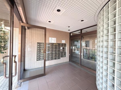 ガラスブロックの曲線壁が特徴的な明るいエントランスです。郵便受けが整然と配置され清潔感が感じられます。大きなガラス扉で開放感があります。