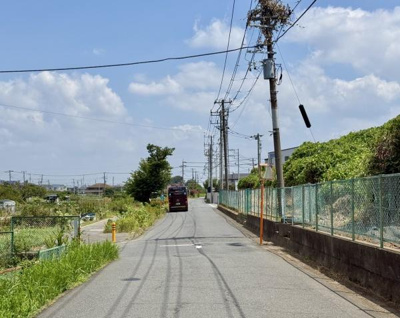開放感のある道路沿いの景観が魅力的です。両側にはフェンスが設置されており安心感があります。空が広く感じられるロケーションとなっています。電線や電柱が整然と配置されています。