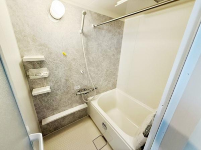 グレーのアクセントパネルがシンプルで落ち着いた印象のバスです。壁付けの棚が備わっており収納スペースが確保されています。浴槽とシャワーの位置も使いやすい配置です。清掃しやすいフラットな床面も特徴です。