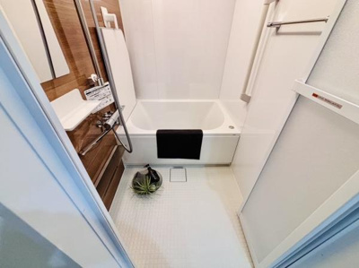 浴槽と洗い場がしっかりと分かれているバスルームです。清潔感のある内装で使いやすいスペースとなっています。収納棚や手すりが設置されている点も便利です。木目調のアクセントパネルが印象的です。