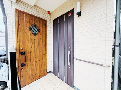 木目調のドアとモダンな玄関扉が印象的です。手すり付きで安心感があります。明るいタイルで清潔感が感じられます。玄関スペースがゆったりしています。外壁も落ち着いた色合いが魅力です。