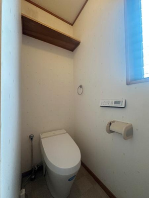 清潔感のあるトイレ空間です。窓があり明るい自然光が差し込みます。壁面には収納棚が設置されています。操作パネルも使いやすい位置にありシンプルなレイアウトです。