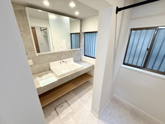 広々とした洗面台が設置されており明るい照明と大きな鏡が空間をすっきりと見せています。二面の窓から自然光が差し込むため朝の準備にも便利です。下部には収納スペースもあり機能性が備わっています。