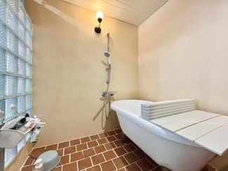 ガラスブロックの壁が印象的なバスルームです。ブラウンのタイル床が落ち着いた雰囲気を演出しています。広めのバスタブが設置されており使い勝手に配慮されています。照明の位置にもこだわりが感じられます。