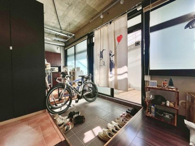 広々とした玄関スペースが印象的です。暗色のタイルと収納扉が全体を引き締めています。大きな窓から光が入り明るさを感じられます。自転車も室内に置けるゆとりがあります。ディスプレイ棚も設置しやすい空間です。