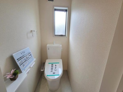 シンプルなデザインのトイレ空間です。窓付きで明るさを取り入れることができます。ペーパーホルダーや棚も備えられています。清潔感のある色合いが特徴です。