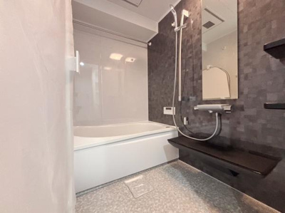 落ち着いた色調の壁面が特徴的なバスルームです。広々とした浴槽がありゆとりを感じられます。シャワーや棚も使いやすく配置されています。清潔感あふれる空間です。