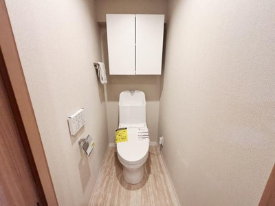 収納棚が設置されておりトイレ用品の整理に便利です。壁付けリモコンで使いやすさも考えられています。明るい色合いの床と壁が空間を広く見せています。シンプルなデザインが特徴的です。