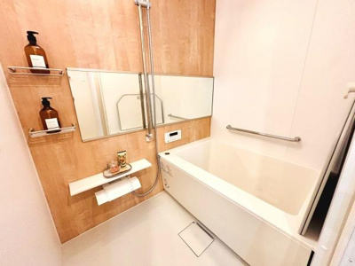 清潔感のあるバスルームです。壁面収納や棚があり使いやすい工夫がされています。木目調のアクセントパネルが落ち着いた雰囲気を演出しています。手すりも設置されているので安心です。