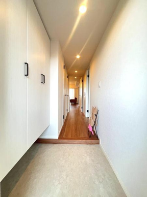 玄関には収納スペースが備わっておりすっきりとした印象です。明るい照明が廊下を照らしており清潔感があります。床面もフラットで安全に配慮されています。奥まで見通しの良い空間です。