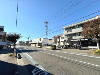道路沿いに店舗や建物が並ぶ開放的な眺めが広がっています。建物の1階には飲食店が入っており利便性も感じられます。青空が広がる明るい通りで周辺の街並みに溶け込んだ環境です。