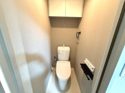 明るい照明が印象的なトイレです。壁付け収納で空間を有効活用しています。ペーパーホルダーやリモコンなど機能的な設備が整っています。清潔感のある配色が特徴です。