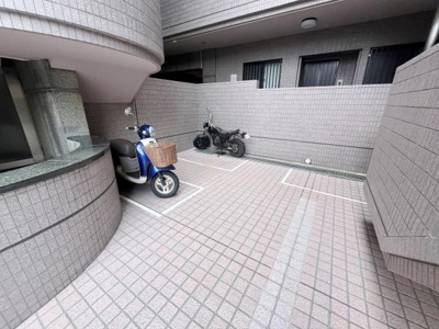 建物の一角にあるバイク置き場はタイル敷きで清潔感があります。区画がしっかりと分けられており安心して利用できます。雨風に強そうな設計が特徴的です。防犯面にも配慮されている印象です。