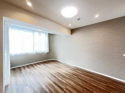 大きな窓から自然光がたっぷり差し込む洋室です。天井にはダウンライトとシーリングライトが配置され明るさも十分です。木目調のフローリングが印象的で落ち着いた雰囲気を演出します。